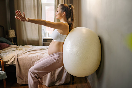 Pregnant woman standing with her back against an exercise ball on a wall